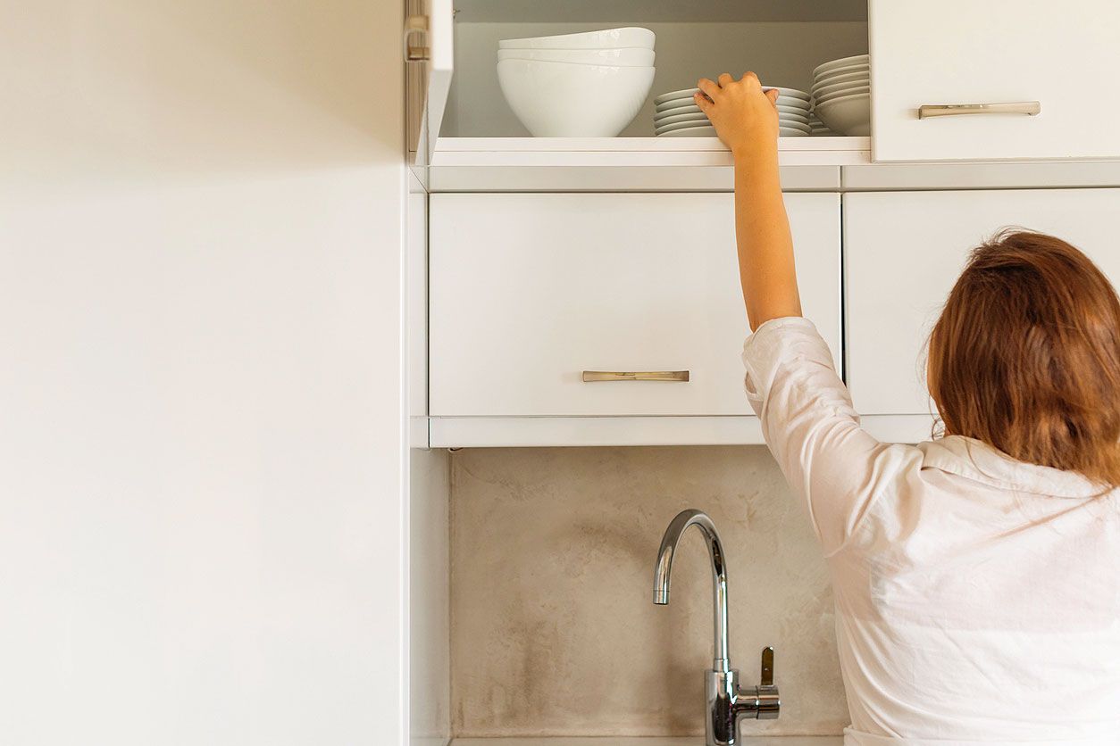 An image of a woman getting a dish from a kitchen cabinet