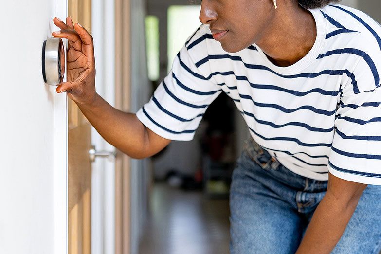 An image of a woman adjusting the thermostat