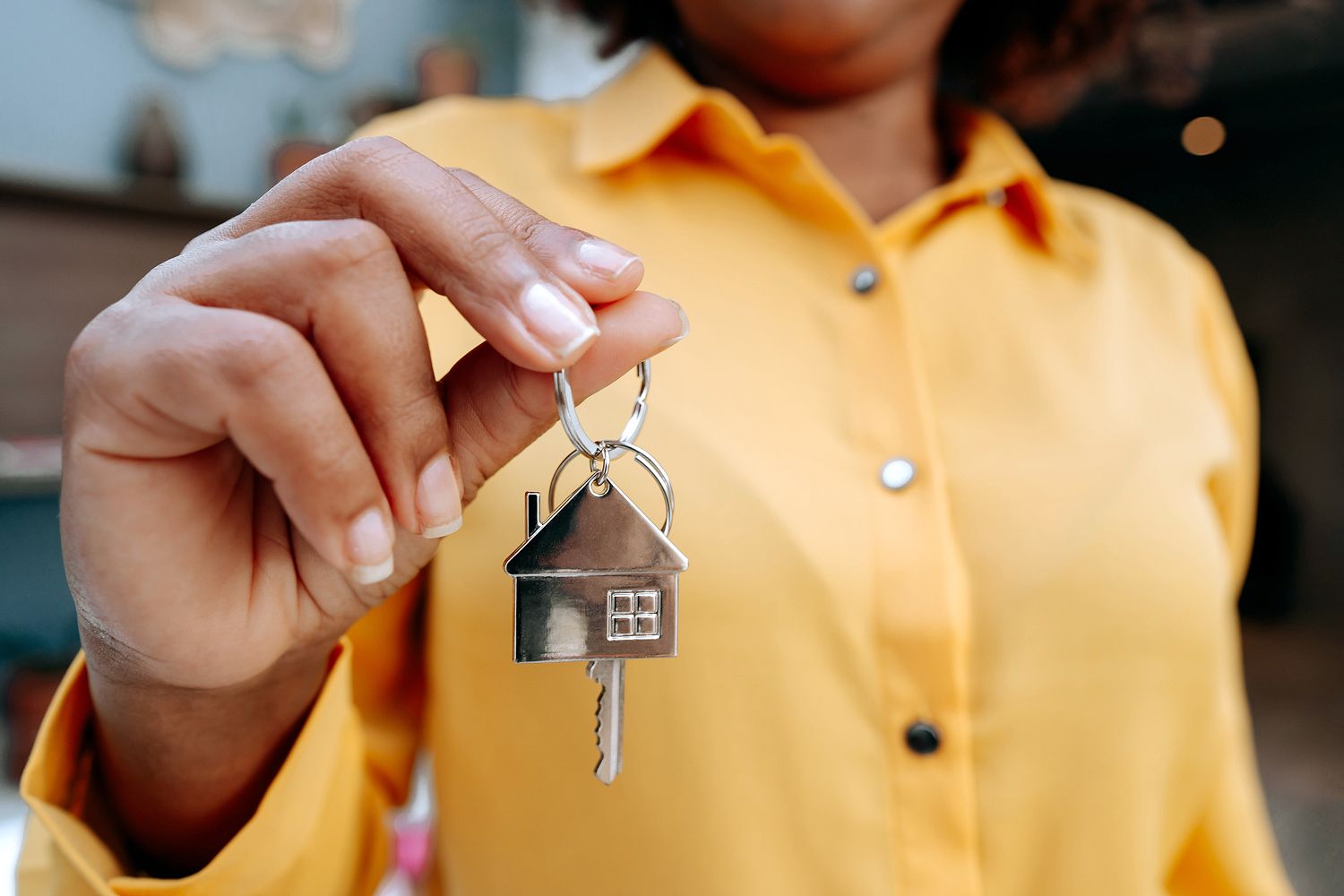 An image of a woman in a yellow shirt holding a keychain of a house