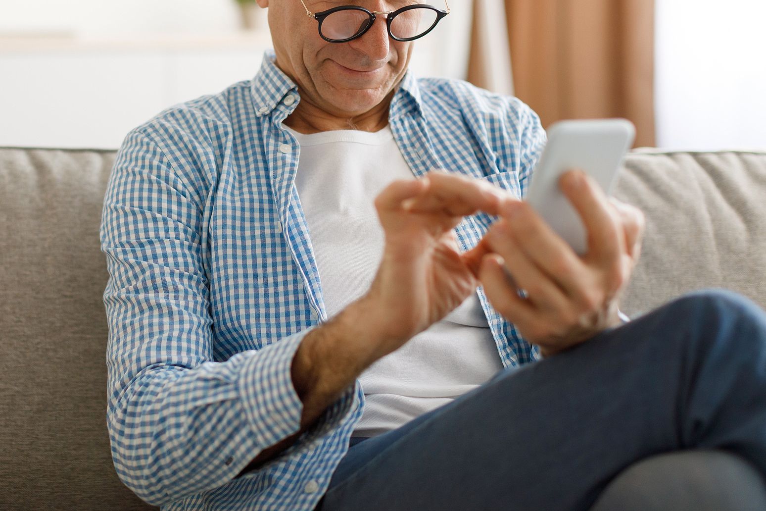 An image of a man typing on his phone while sitting on a couch