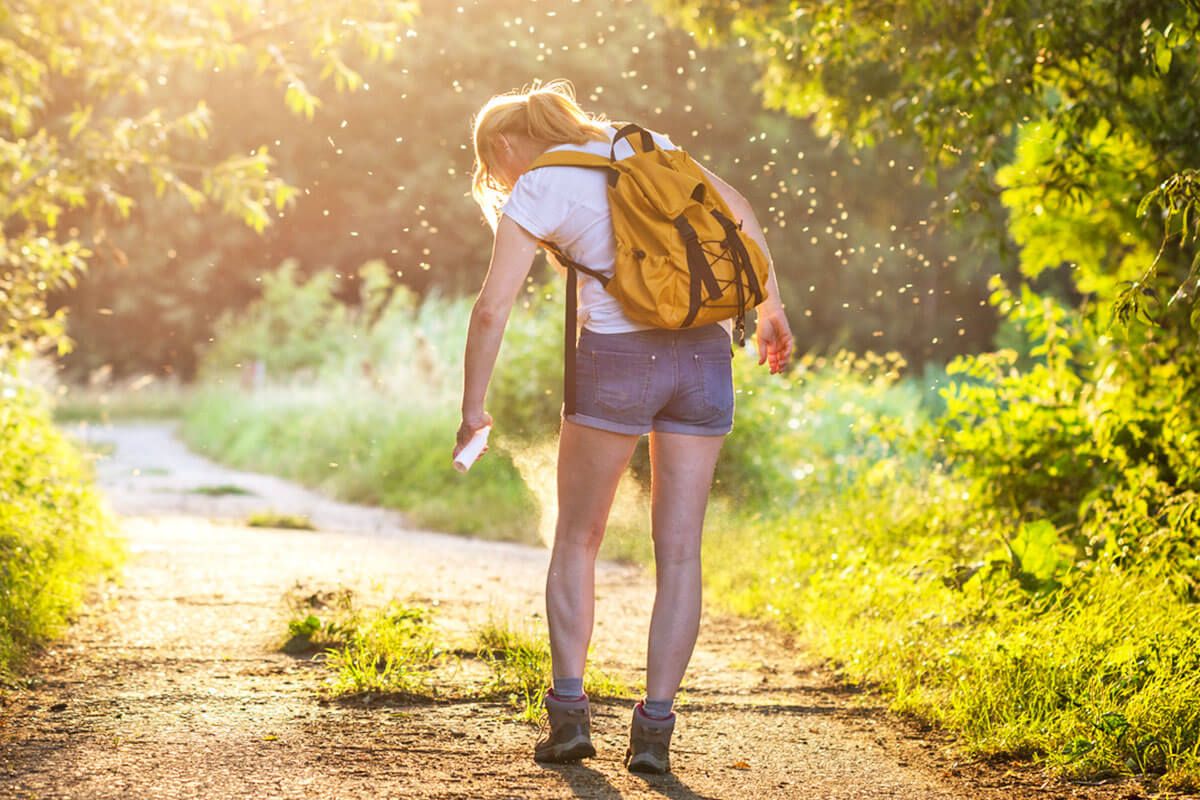 Woman with a backpack spraying bug spray to keep bugs away