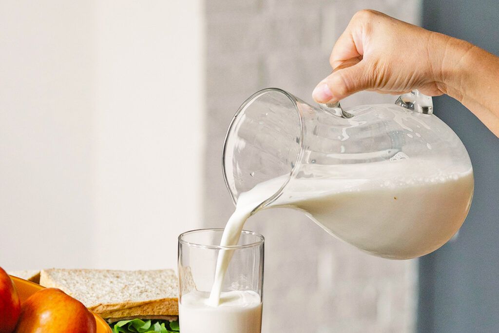 Person pouring milk from jug into glass