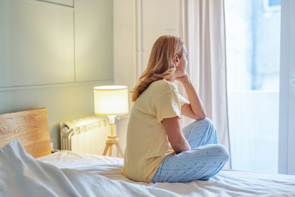 Woman sitting on bed looking out window