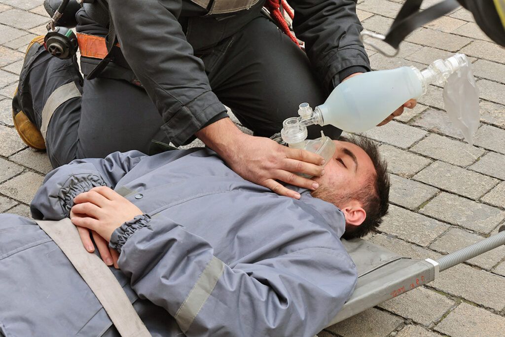 Firefighter putting oxygen bag over mouth of man on the ground