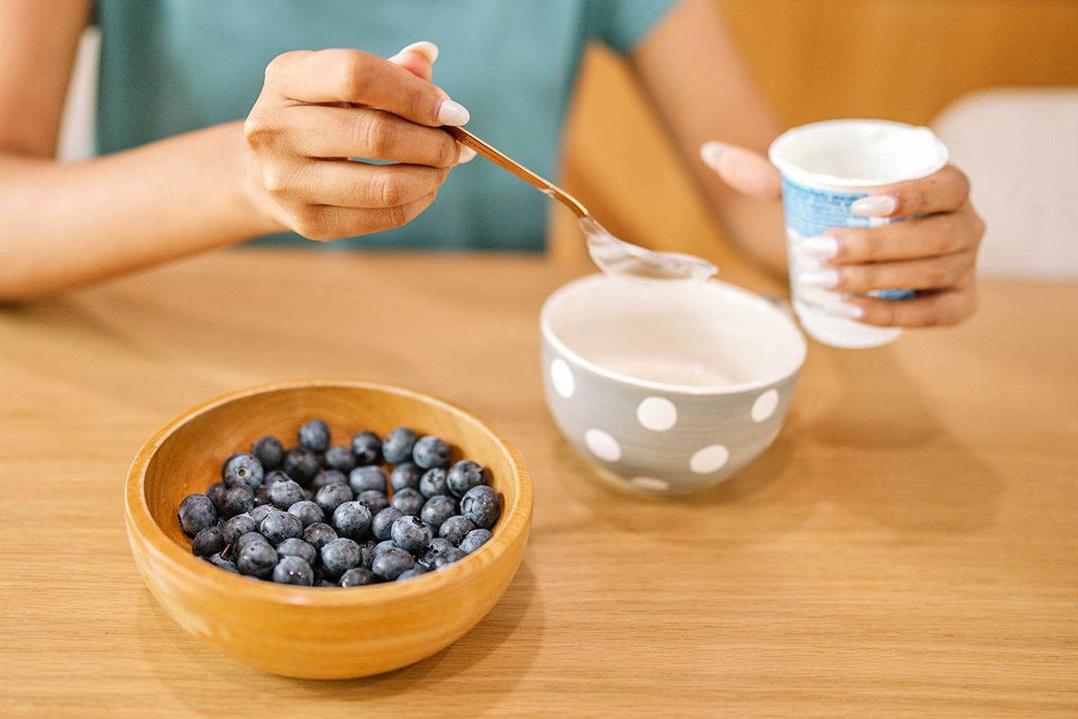 Hands holding yogurt with blueberries in a bowl on the side