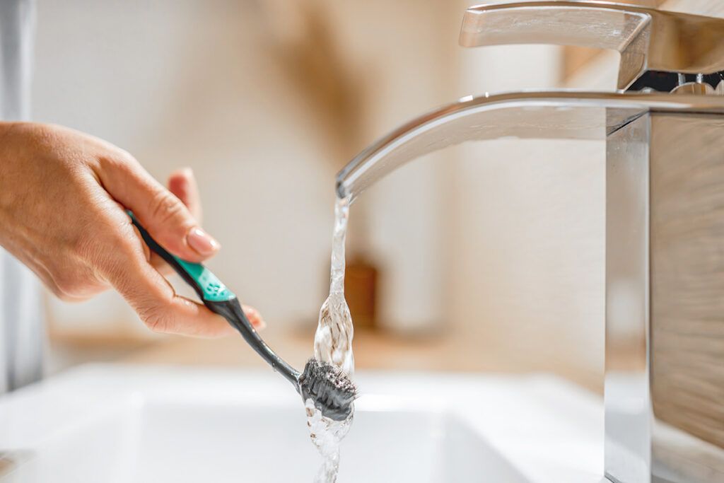 Hand holding toothbrush under running water